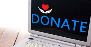 laptop on a table. the screen on the laptop has "donate" with a pair of hands holding a heart. 