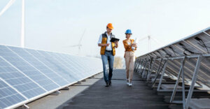 two people walking in between solar panels on a roof. They are wearing construction hats.