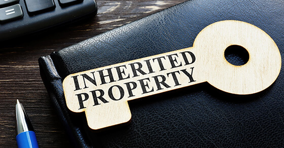 outline of a key on top of a briefcase on a table. The key has the words "Inherited Property" on it.