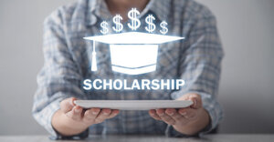 individual holding a piece of paper with a graphic of a graduation cap and money symbols with the word "scholarship".