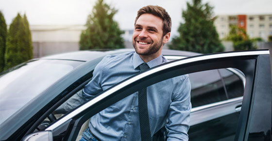 Image of a smiling individual getting out of a car.