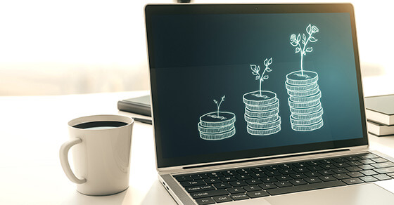 image of an open laptop with a screen that has three sets of coins displayed in a tower (less to more coins at the end) and baby plants growing out of the tops of the coins.