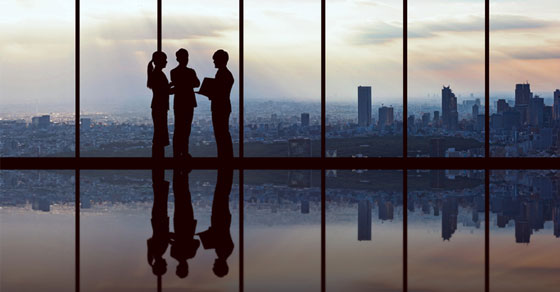 silhouette of business professionals in the evening in front of windows with the city skyline in the back.