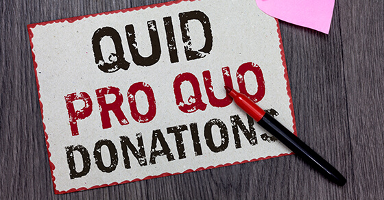 Image of a paper on a desk with the words "QUID PRO QUO DONATIONS" on it and a red pen on the desk next to it. The words "PRO QUO" were in red, the other words were in black ink.