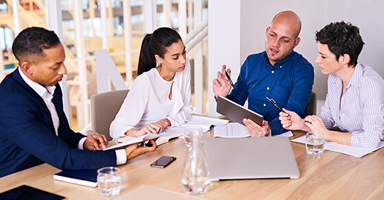 image of people sitting around a table, in a meeting, with work papers.