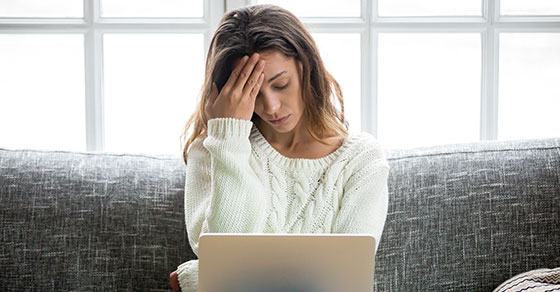 image of an individual holding their head in concern while viewing a laptop screen