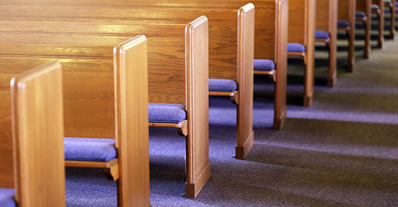 Window light is shing on rows of empty church pews in a Church Sanctuary without any people in it.
