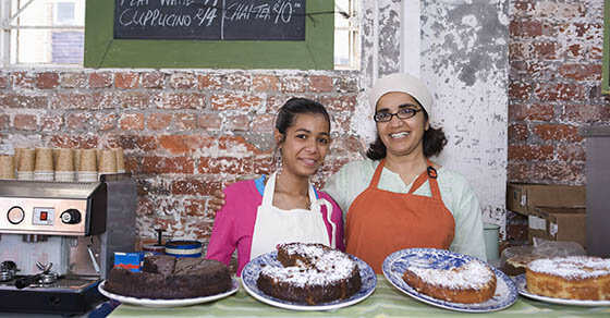 Portrait of happy mother and daughter in aprons standing at cake shop counter