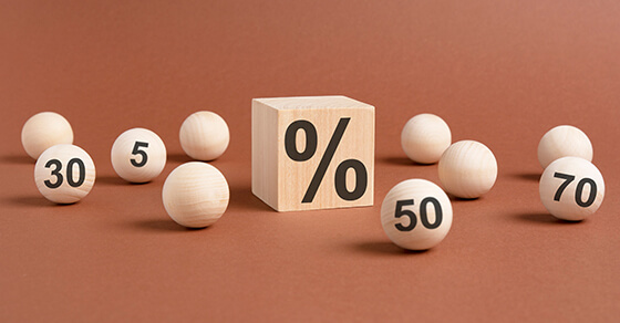 one wooden cube with percent symbol printed and many wooden balls with with numbers 5, 30, 50, 70, viewed in close-up with shadow on brown background