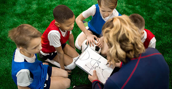 Football instructor drawing scheme of moving during soccer game or training and explaining it to group of boys
