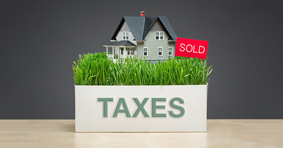 image of a model house in a box labeled "taxes" and a sold sign. The box is on a table.