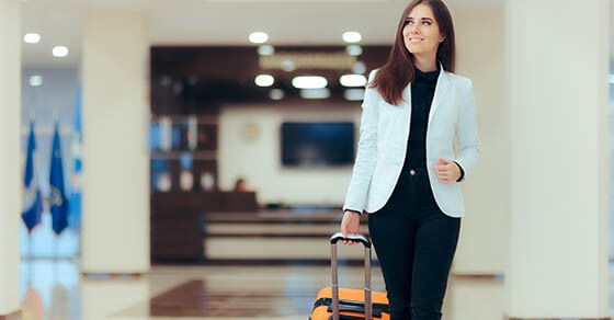 Elegant Business Woman with Travel Trolley Luggage in Hotel Lobby. Female executive with suitcase in work related business trip