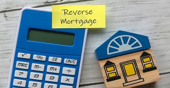 images of a calculator and a house on a desk with a postit that reads "reverse mortgage"