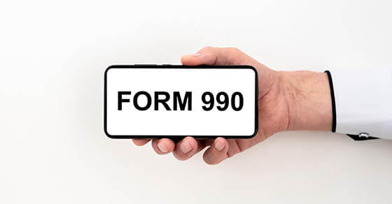 form 990 inscription on the screen of the phone that the hand holds on a white background. Tax form concept. Electonic taxation concept