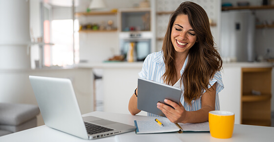 Image of an individual smiling while looking at paperwork on a table with an open laptop.