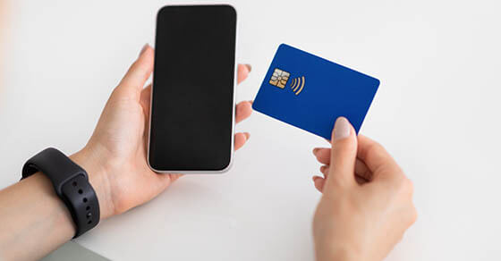 Hands of young european woman use smartphone with blank screen and credit card on white table in office, cropped. Banking, business and work, device and shopping, sale app, order and pay