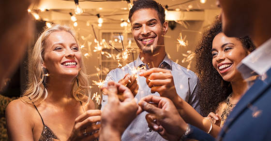 Group of multiethnic friends having fun with sparkling sticks during night party. Group of elegant women and men holding sparklers and celebrating the new year’s eve.